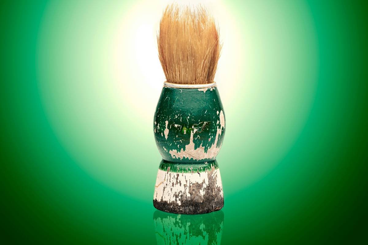 Hand holding classic shaving brushes creating rich lather in ceramic bowl